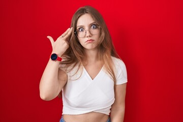 Young caucasian woman standing over red background shooting and killing oneself pointing hand and fingers to head like gun, suicide gesture.