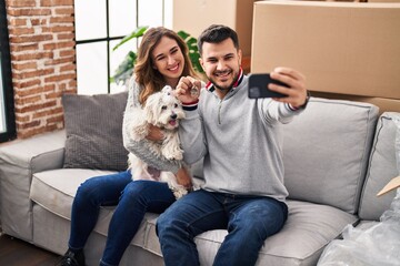 Man and woman make selfie by the smartphone sitting on sofa with dog at new home