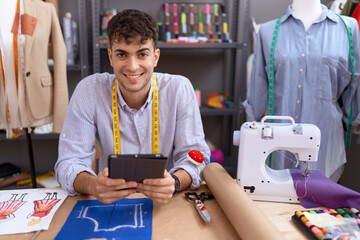Young hispanic man tailor smiling confident using touchpad at atelier