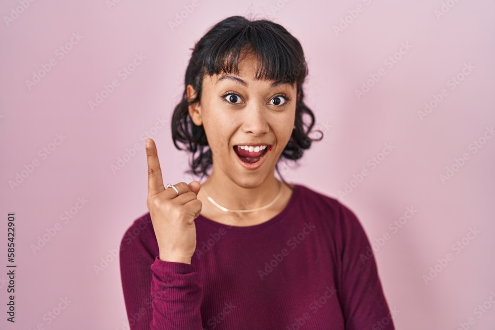 Poster Young beautiful woman standing over pink background pointing finger up with successful idea. exited and happy. number one.