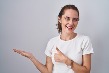 Beautiful brunette woman standing over isolated background showing palm hand and doing ok gesture with thumbs up, smiling happy and cheerful