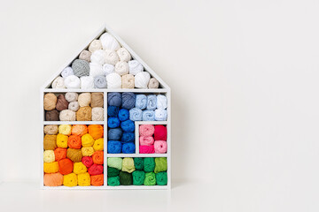 White house shaped shelving with colored balls of yarn for knitting. Bright yarn balls lined up on the shelves. Organizing and storage in craft room. Handmade, needle craft, creativity and  hobby.
