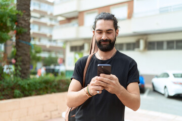 Young hispanic man musician using smartphone holding guitar case at park