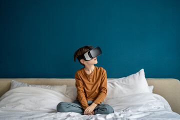 Interested kid boy using futuristic VR goggles interacting with virtual reality metaverse while...