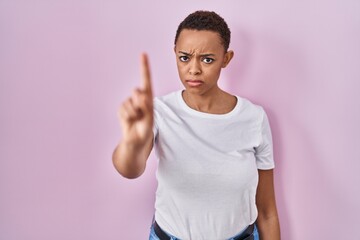 Obraz premium Beautiful african american woman standing over pink background pointing with finger up and angry expression, showing no gesture