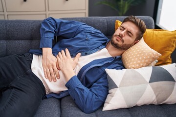 Young caucasian man suffering for stomach ache lying on sofa at home