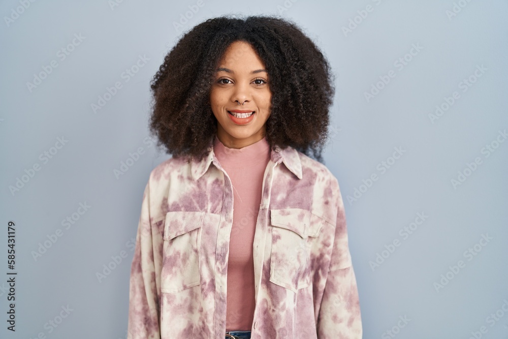 Sticker Young african american woman standing over blue background with a happy and cool smile on face. lucky person.