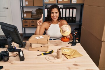 Young hispanic woman working at small business ecommerce worldship smiling with an idea or question pointing finger with happy face, number one