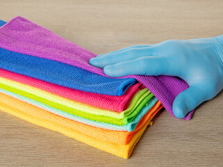 Hand in a blue glove selects a towel from a stack of bright microfiber towels for cleaning