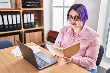 Young beautiful plus size woman business worker using laptop writing on notebook at office