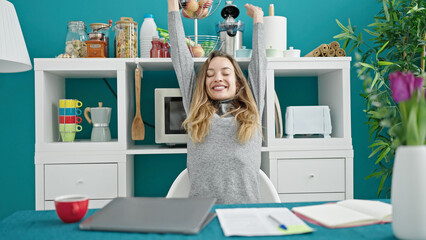 Young caucasian woman using laptop with arms open at dinning room