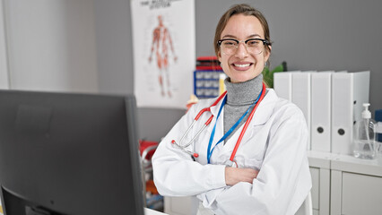 Young caucasian woman doctor using computer sitting with arms crossed gesture at clinic