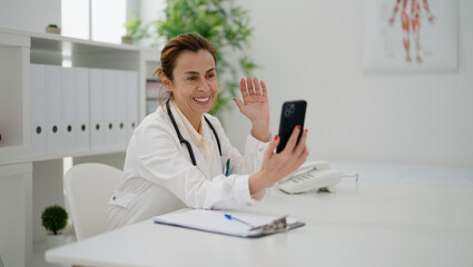 Middle age hispanic woman wearing doctor uniform having video call at clinic