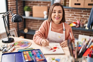 Fototapeta premium Middle age woman artist drawing on notebook at art studio