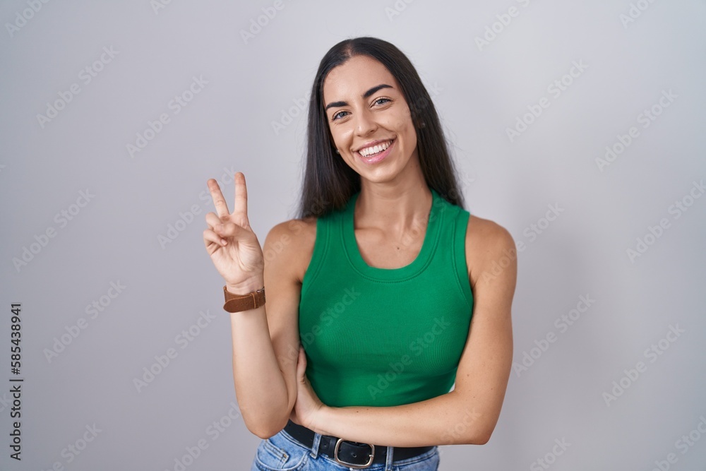 Sticker young woman standing over isolated background smiling with happy face winking at the camera doing vi