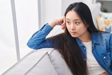 Young chinese woman sitting on sofa with serious expression at home