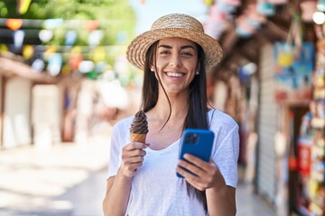 Young hispanic woman tourist using smartphone eating ice cream at street market