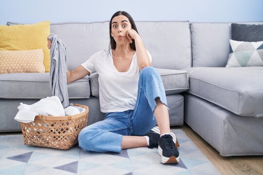 Young brunette woman doing laundry at home making fish face with mouth and squinting eyes, crazy and comical.