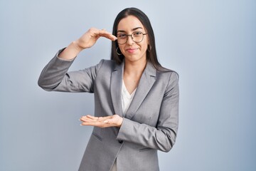 Hispanic business woman wearing glasses gesturing with hands showing big and large size sign, measure symbol. smiling looking at the camera. measuring concept.