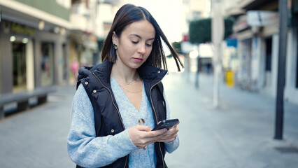 Young beautiful hispanic woman using smartphone with serious expression at street