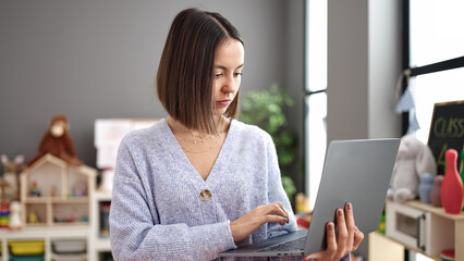 Young beautiful hispanic woman working as a teacher using laptop at kindergarten