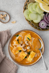Paneer Butter Masala or Indian Cottage Cheese Curry served in a bowl with rice, fresh vegetables and paratha. Flat lay