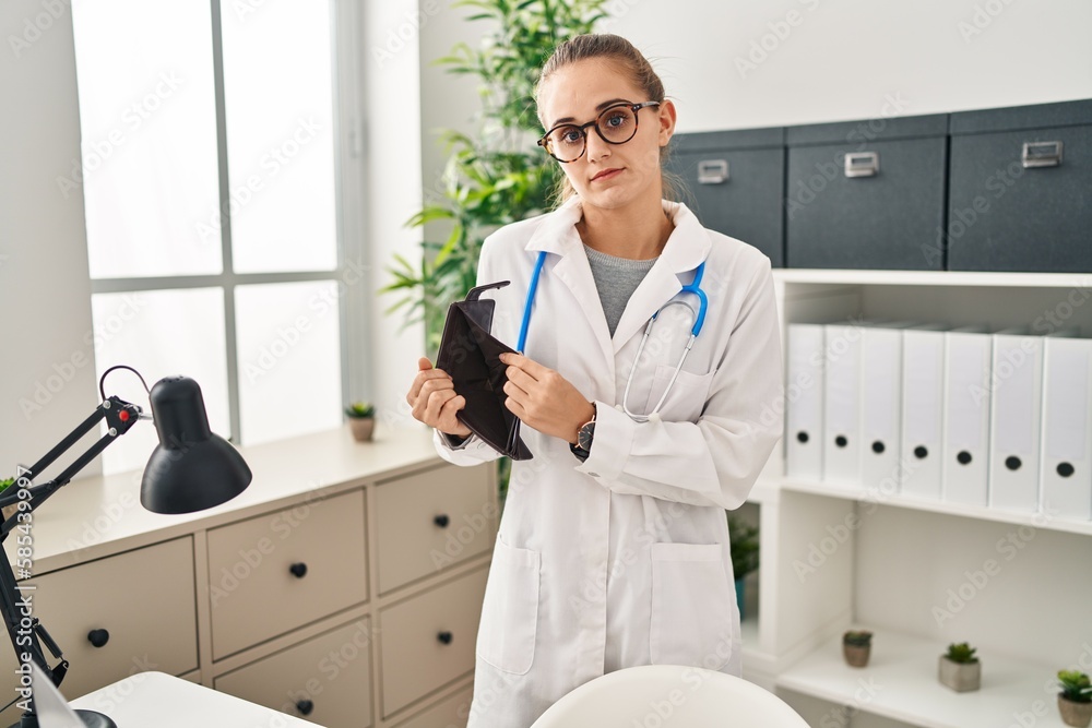 Canvas Prints young blonde woman wearing doctor uniform showing empty wallet at clinic