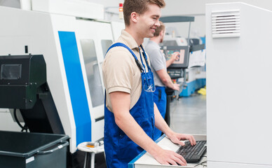 Worker using keyboard to enter data into a manufacturing machine on factory floor