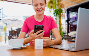 Woman using contactless payment by mobile phone with QR code at cafe