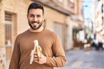Young hispanic man smiling confident eating banana at street