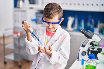 Blond child wearing scientist uniform using pipette at laboratory