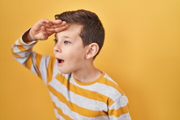 Young caucasian kid standing over yellow background very happy and smiling looking far away with...