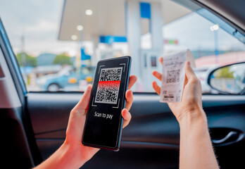 Woman using contactless payment by mobile phone with QR code at car filling station