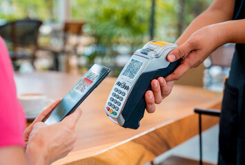 Woman using contactless payment by mobile phone with QR code at cafe