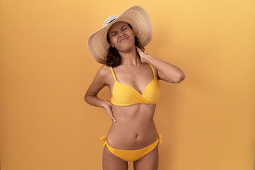 Young hispanic woman wearing bikini and summer hat suffering of neck ache injury, touching neck with hand, muscular pain