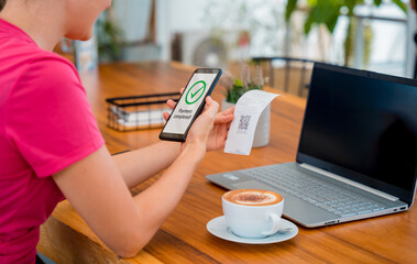 Woman using contactless payment by mobile phone with QR code at cafe