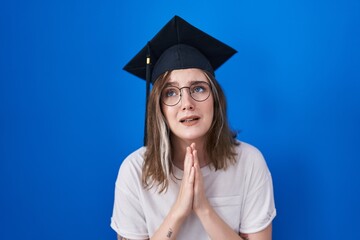 Blonde caucasian woman wearing graduation cap begging and praying with hands together with hope expression on face very emotional and worried. begging.