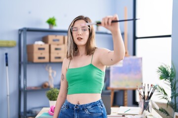 Young woman artist holding paintbrush at art studio