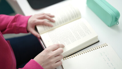 Young blonde woman student reading book sitting on table at library university