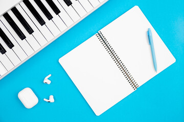 Blank notebook and piano on blue background, top view, concept of musical creativity and education, white synthesizer, flat lay.