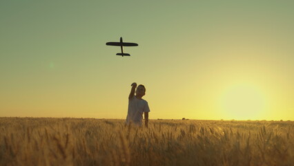 Kid aviator. Happy child throws toy plane with his hand on field, sunset. Teenager dreams of flying becoming pilot. Boy child wants to become pilot, astronaut. Slow motion. Children play toy airplane