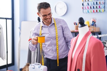 Young hispanic man tailor smiling confident drinking coffee at tailor shop