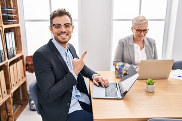 Hispanic young man working at the office smiling happy pointing with hand and finger