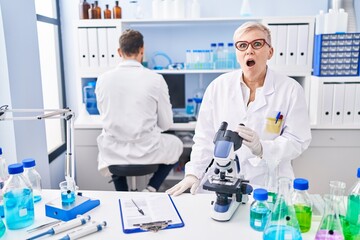 Middle age woman working at scientist laboratory scared and amazed with open mouth for surprise, disbelief face