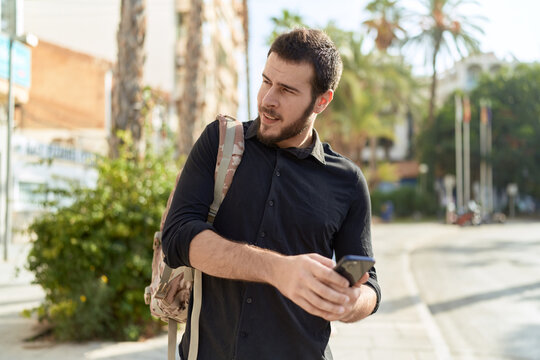 Young hispanic man using smartphone wearing backpack at street