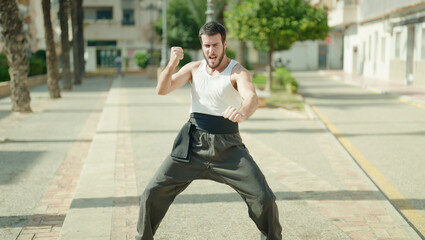 Young hispanic man karate fighter training at park