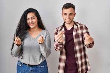 Young hispanic couple standing over white background doing money gesture with hands, asking for salary payment, millionaire business