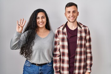 Young hispanic couple standing over white background showing and pointing up with fingers number four while smiling confident and happy.