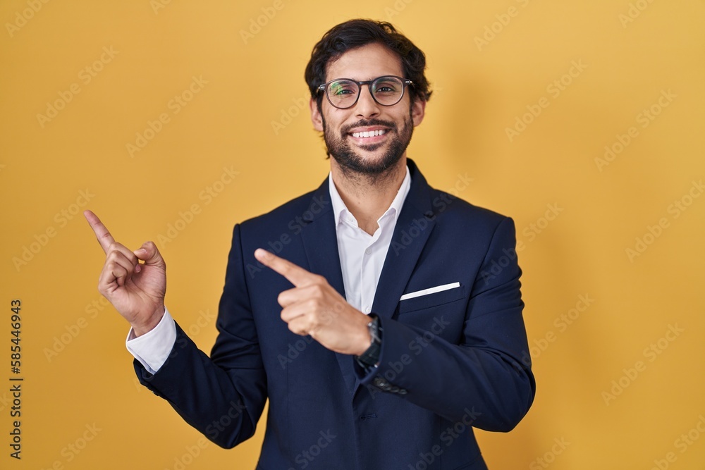 Poster handsome latin man standing over yellow background smiling and looking at the camera pointing with t