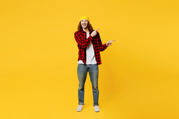 Full body young man wearing red checkered shirt white t-shirt hat point index finger aside indicate on workspace area copy space mock up isolated on plain yellow background studio. Lifestyle concept.